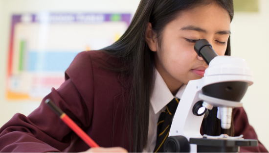 Girl in school uniform looking into microscope in a classroom