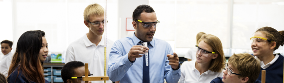 An image of a teacher demonstrating a science practical, with surrounding students watching